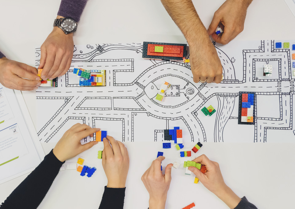 Mehrere Personen gestalten gemeinsam ein Modell mit LEGO Bausteinen auf einem Straßenplan.